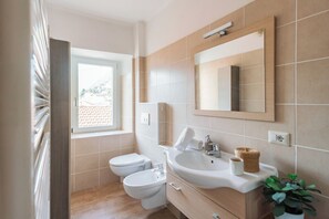 Un baño con inodoro, bidé, lavamanos, espejo y ventana.