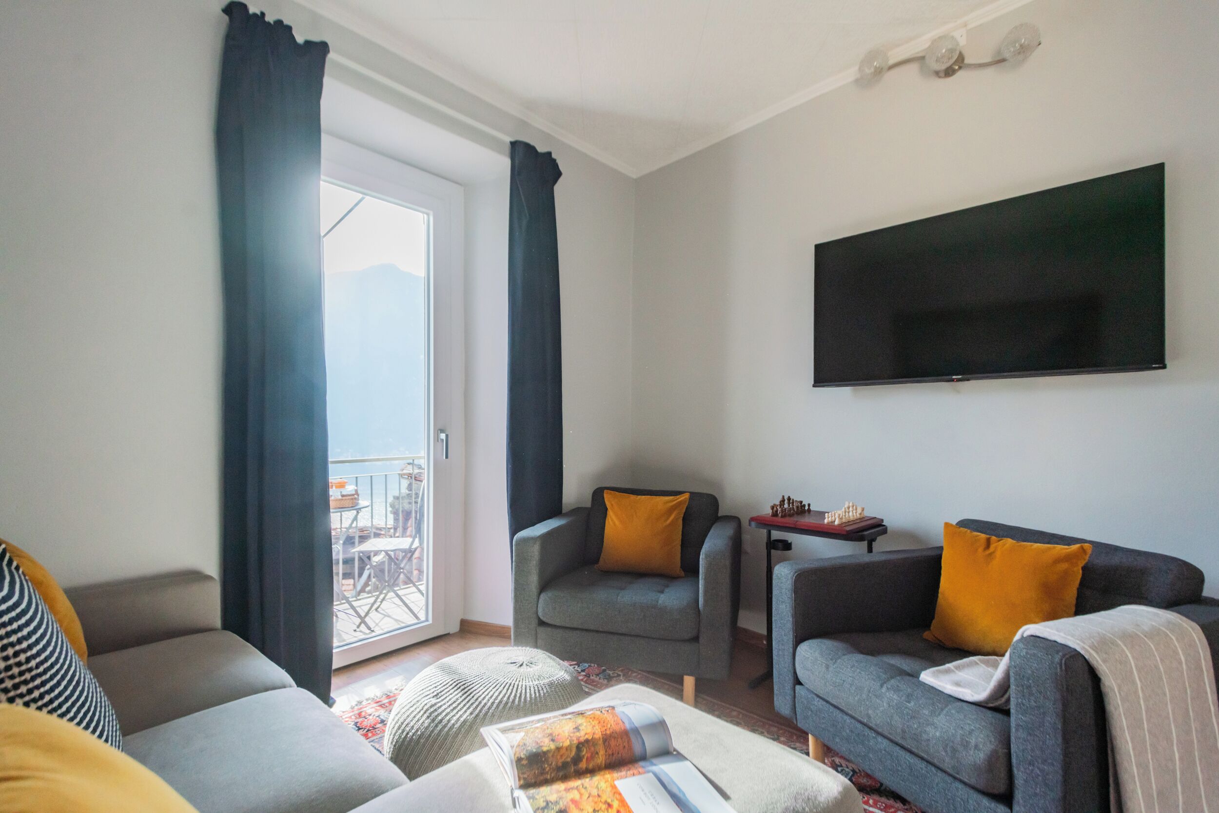 Una sala de estar moderna con sofá, sillón, reposapiés, televisor de pantalla plana y un tablero de ajedrez.