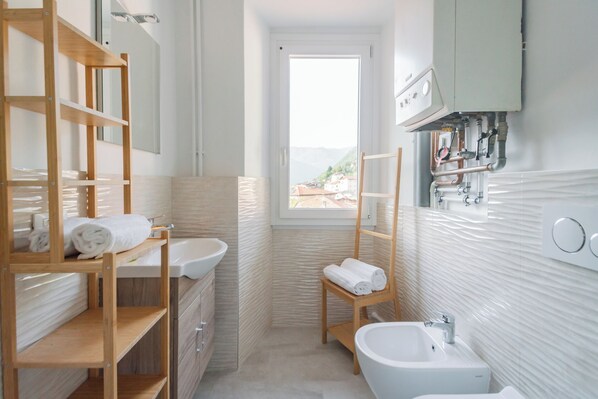 A bathroom with a wooden shelf, a sink, a bidet, and a window with a view. - Villetta Panebianco Home in Castagna 11 by Rent all Como (Nesso)