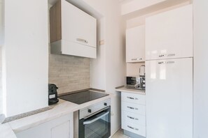 Una cocina compacta con armarios blancos, horno integrado, microondas y cafetera.