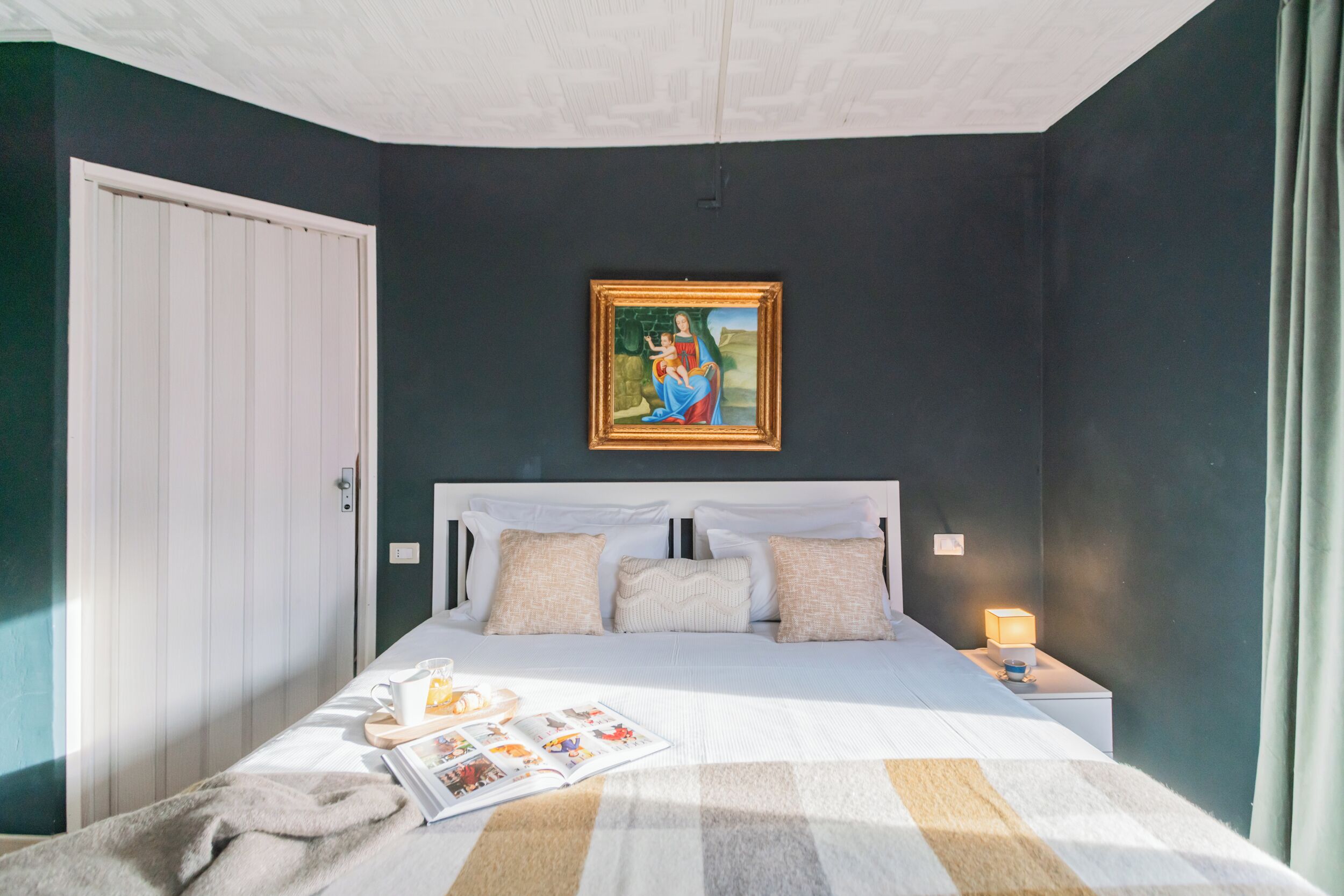Une chambre à coucher comprenant un lit, une table de chevet, une lampe de chevet, un tableau encadré accroché au mur et une porte.