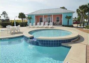 A swimming pool with a waterfall feature, surrounded by lounge chairs and a small building with a tiled roof. - The Rookery Iii 5008 3 Bedroom Cottage (Gulf Shores)