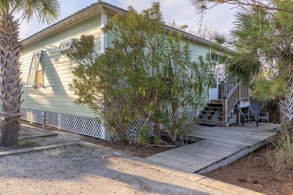 A light green house with a wooden deck, a small porch, and a staircase leading to the front door. - The Rookery Iii 5008 3 Bedroom Cottage (Gulf Shores)