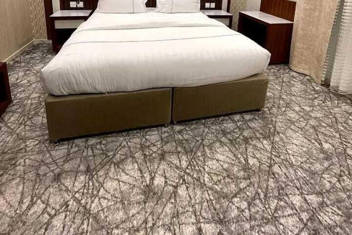 A hotel room with a large bed, two bedside tables, an air conditioning unit, and patterned wallpaper.