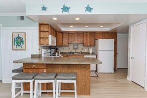 A kitchen with wooden cabinets, a central island with stools, a refrigerator, and decorative turtle wall art.