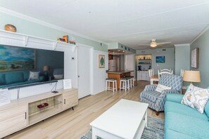 Een woonkamer met een televisie, zitmeubels en een keuken op de achtergrond.