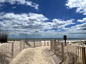 Een zandpad langs het strand met houten omheiningen die naar de oceaan leiden.