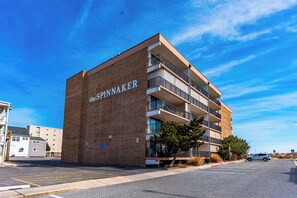 A multi-story building with the name "SPINNAKER" on its facade, featuring balconies and a parking lot in front.