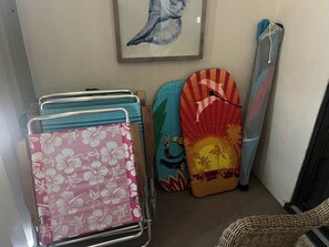 Un étagère de rangement avec des vêtements pliés, une œuvre d’art encadrée et une chaise en osier.