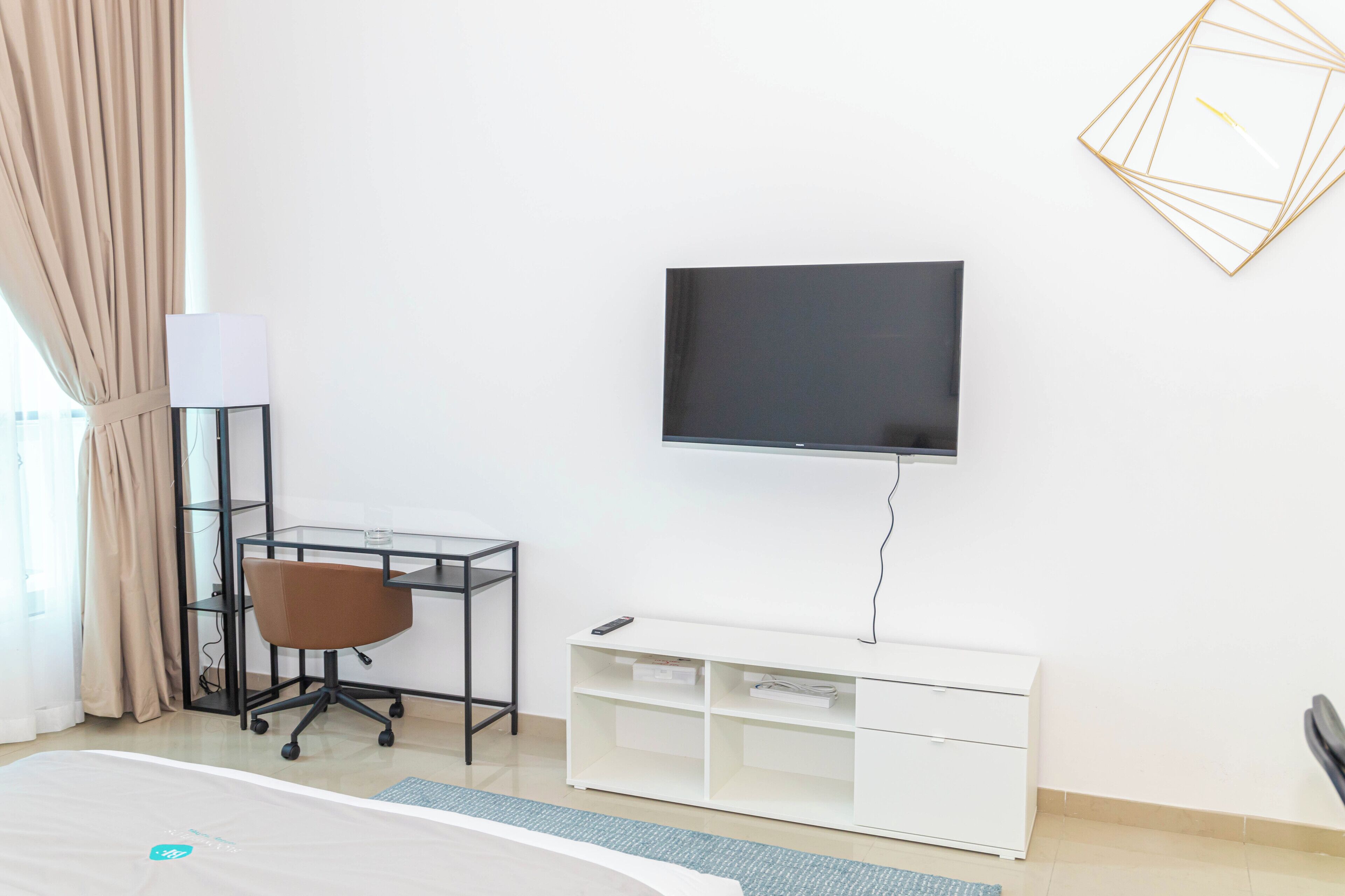 A hotel room with a bed, a desk with a chair, a TV, and a white storage unit.