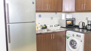 Una cucina compatta con frigorifero in acciaio inox, forno a microonde, lavatrice e mobili in legno.