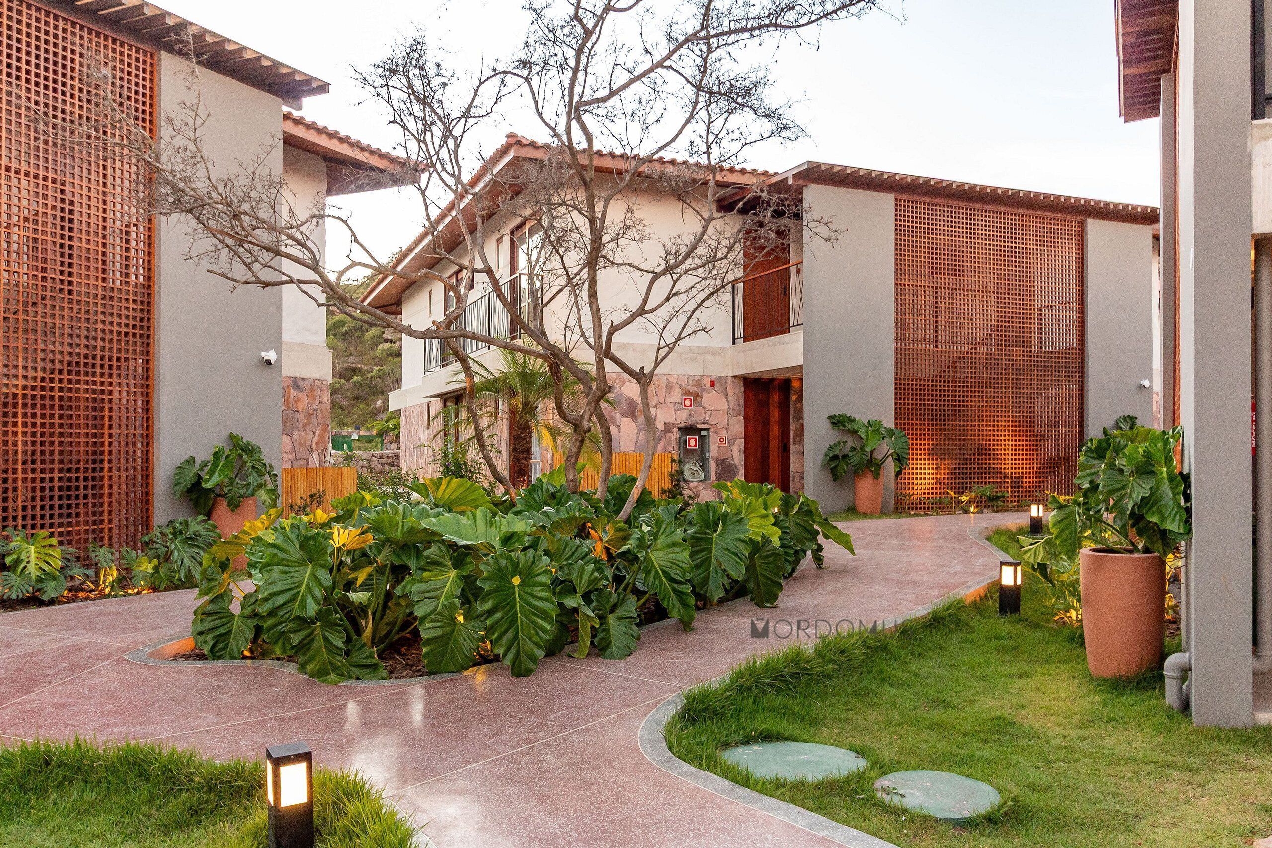 A courtyard with a central pathway, surrounded by lush greenery and potted plants.