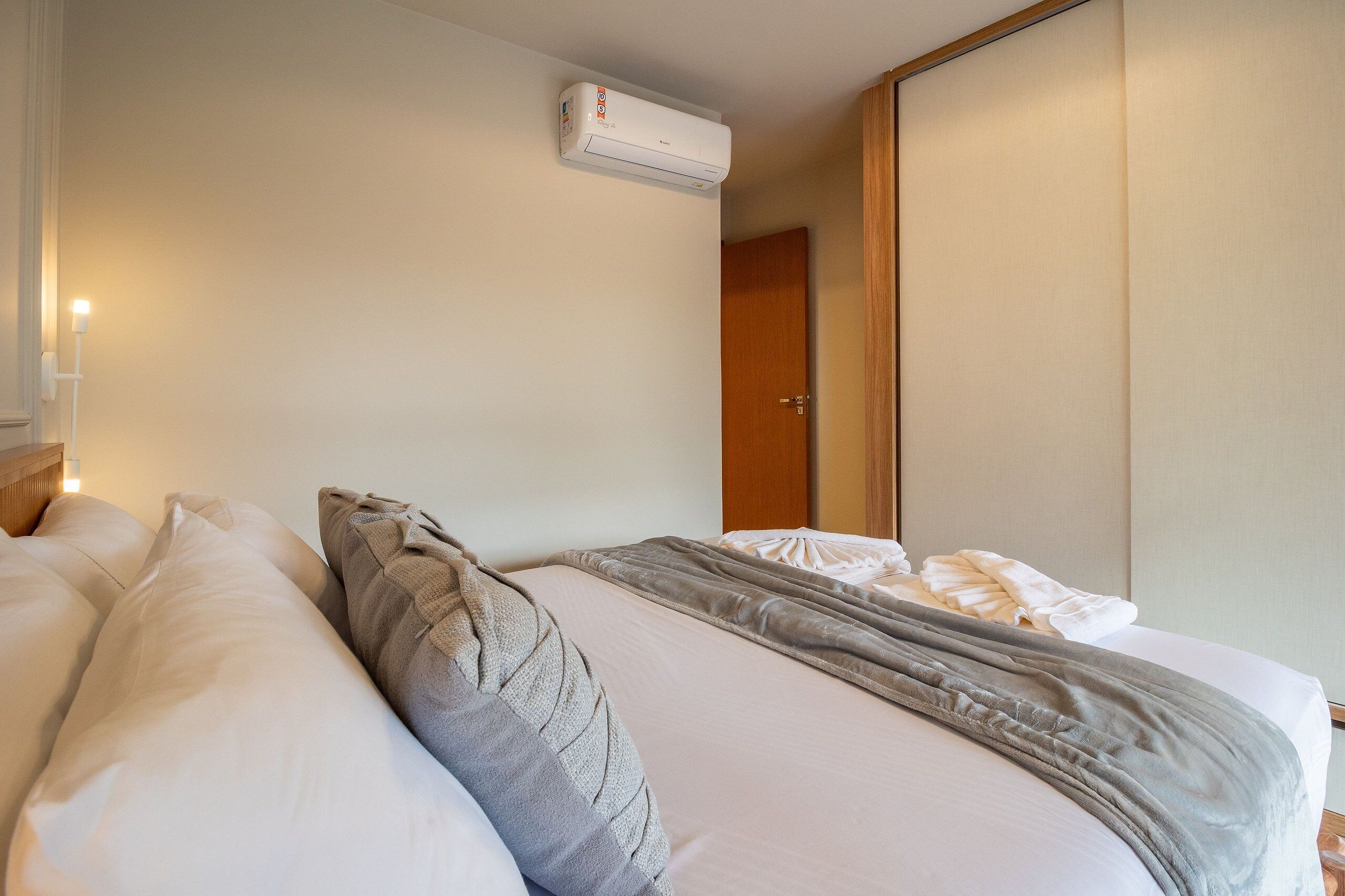 A hotel room with a bed, pillows, a blanket, an air conditioning unit, and a wooden door.