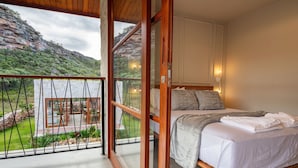 A bedroom with a large bed, a balcony with a view of a mountainous landscape, and a sliding glass door leading to an outdoor area.