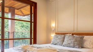 A bedroom with a large window, a wooden bed frame, and a view of greenery outside.