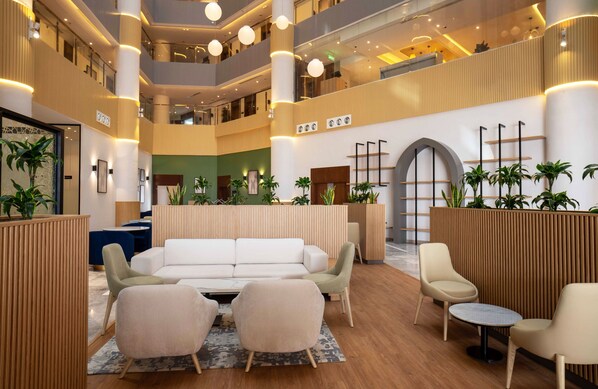 Un hall d’hôtel à plusieurs niveaux, doté d’un espace salon central, de cloisons en bois et de nombreux arrangements floraux.