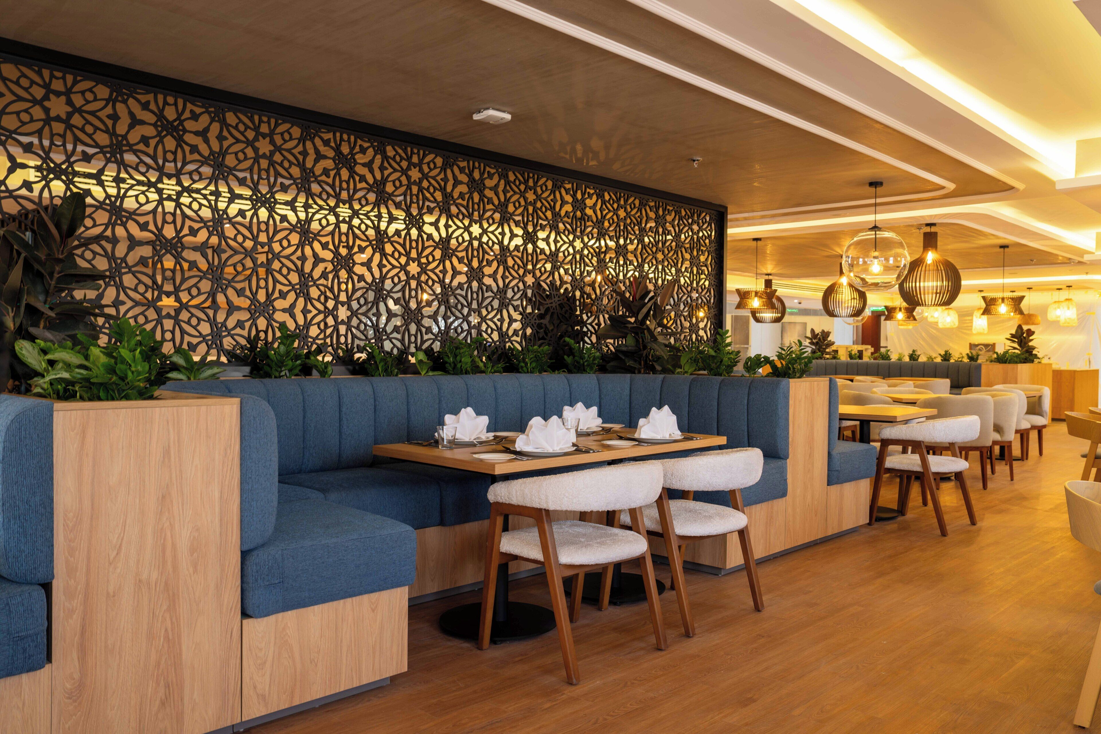A modern restaurant with wooden flooring, blue cushioned seating, and a decorative wall.