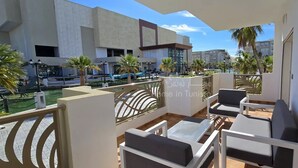 Ein Balkon mit Sitzgelegenheit, ein Pool und moderne Gebäude im Hintergrund.