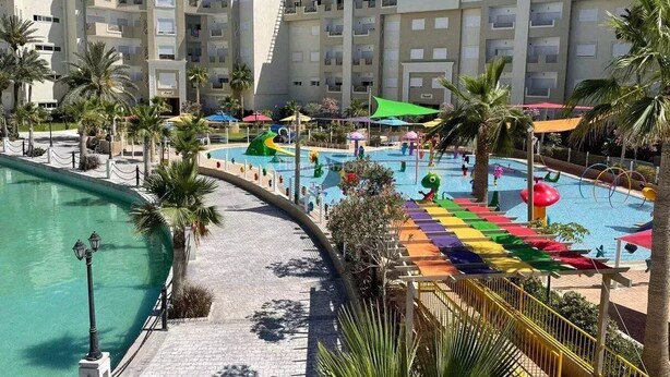Ein Hotel mit Swimmingpool, Palmen und einer bunten Wasserrutsche.
