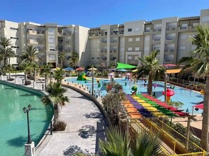 A hotel with a swimming pool, palm trees, and a colorful water slide.