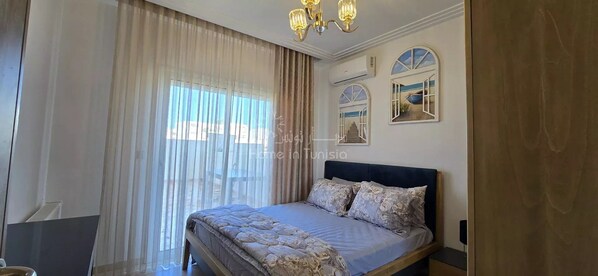 A bedroom with a bed, curtains, a chandelier, and wall art.