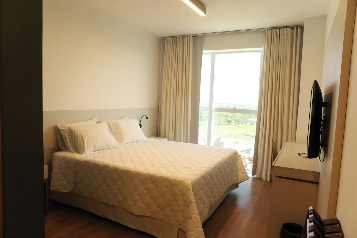 A hotel room with a bed, a TV, and a view of the outdoors.