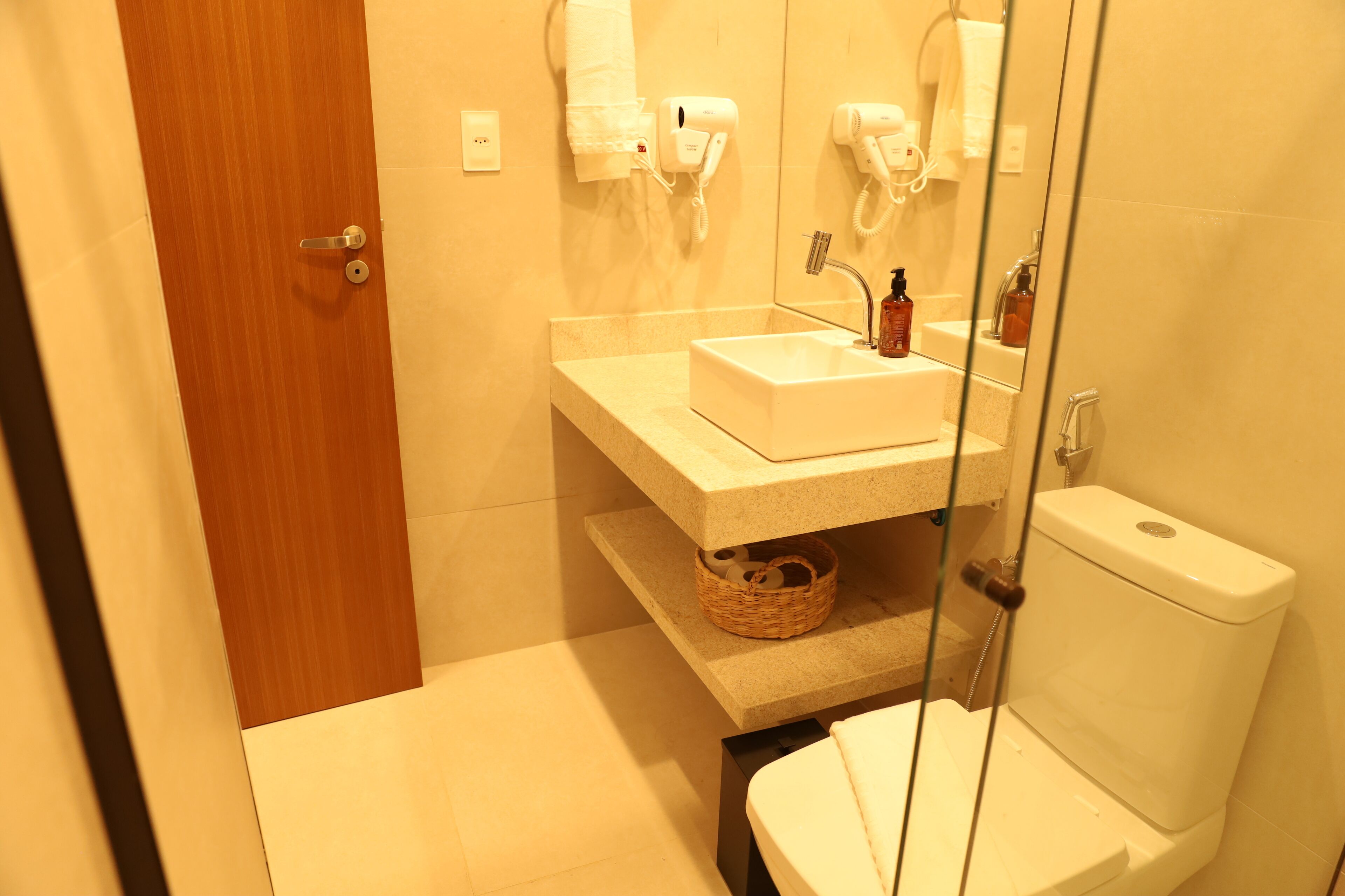 Un baño con puerta de madera, un lavabo blanco, un espejo, un inodoro y una cesta sobre la encimera.