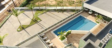 A rooftop swimming pool with lounge chairs and palm trees.