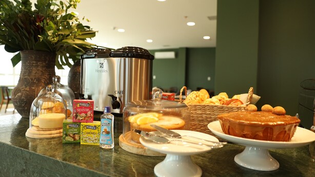 A breakfast buffet with various food items, a coffee machine, and a potted plant. - Palace Green Hotel (Lagarto)