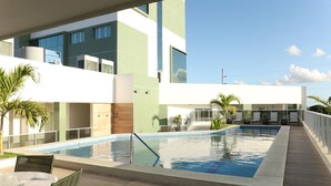 Un hôtel moderne doté d’une grande piscine extérieure, d’un espace détente abrité et offrant une vue sur les bâtiments environnants.