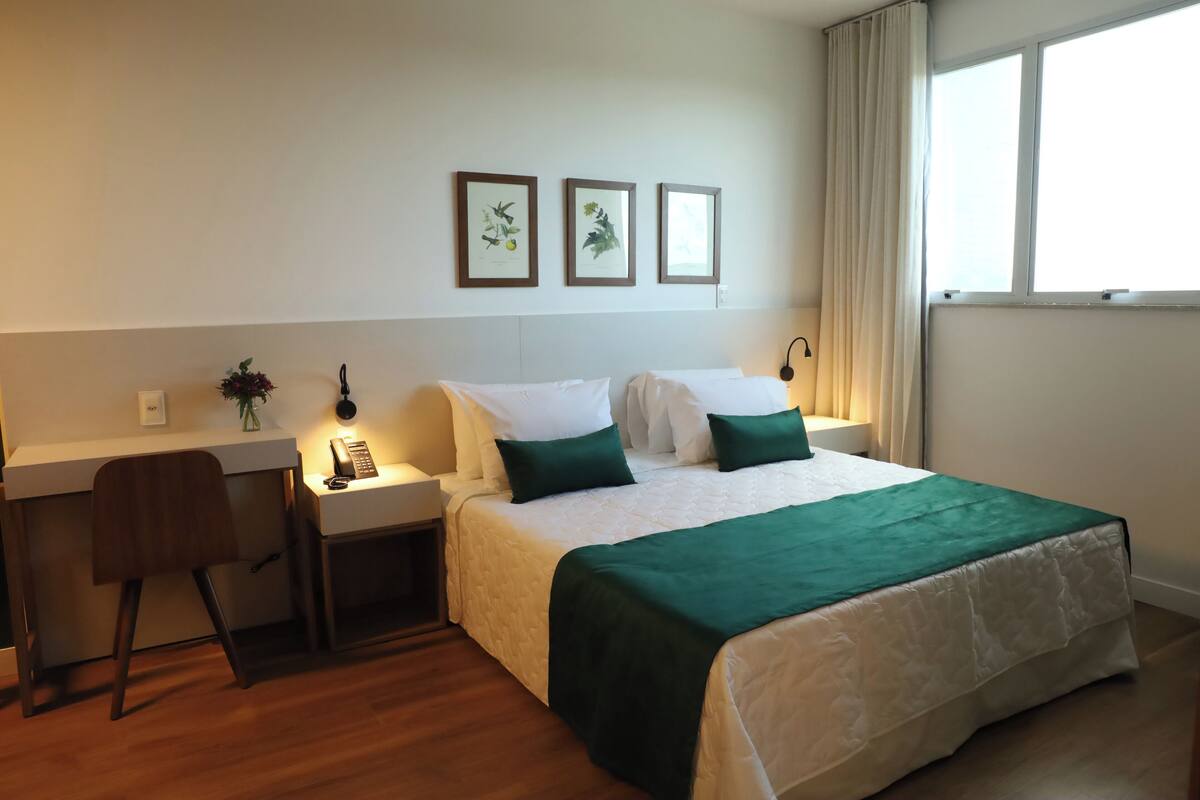 A hotel room with a bed, a desk, a chair, and a window.