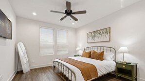 Ein Schlafzimmer mit einem Bett, zwei Nachttischen, einem Deckenventilator und einem an der Wand montierten Fernseher.
