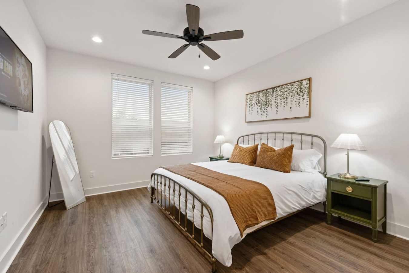 Une chambre à coucher comprenant un lit, deux tables de chevet, un ventilateur de plafond et un téléviseur fixé au mur.