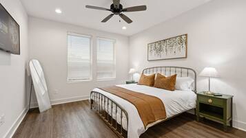 Une chambre à coucher comprenant un lit, deux tables de chevet, un ventilateur de plafond et un téléviseur fixé au mur.