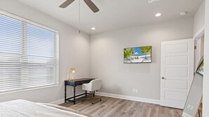 A bedroom with a bed, a desk, a chair, a ceiling fan, and a painting on the wall.