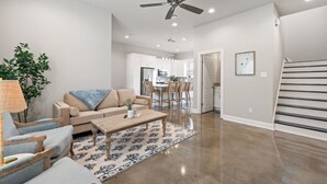A spacious living room with a sofa, coffee table, and chairs, a kitchen in the background, and a staircase.