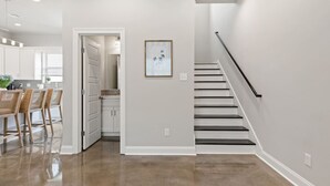 A modern kitchen with white cabinets, a dining area with wicker chairs, and a staircase with a black railing.