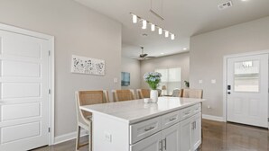 A modern kitchen with white cabinetry, a central island, and a dining area with wicker chairs.