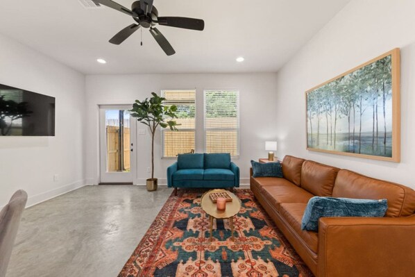 A living room with a ceiling fan, a blue sofa, a brown leather sofa, a patterned rug, and a painting on the wall.