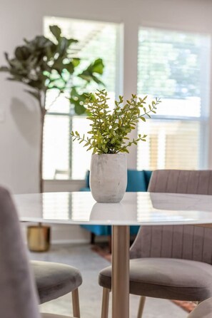 A dining table with a white vase containing green plants, surrounded by grey chairs in a modern interior.