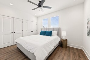 A bedroom with a bed, white walls, a ceiling fan, and a window with blinds.
