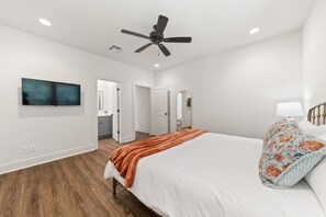 A bedroom with a bed, a ceiling fan, a TV on the wall, and a bathroom visible through an open door.