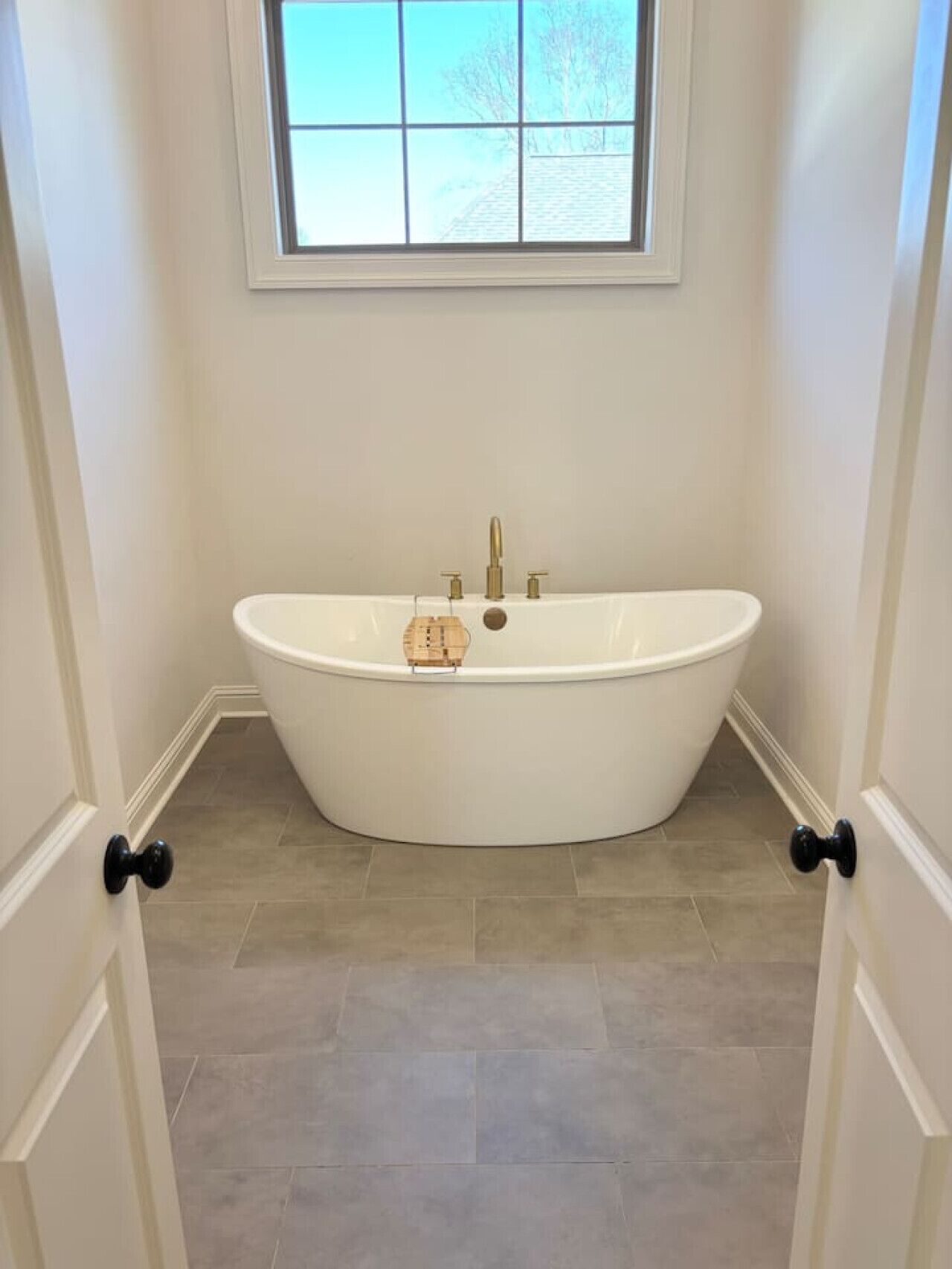 A bathroom with a freestanding bathtub, a window above the tub, and a door with a doorknob.
