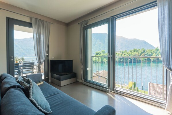 Ein modernes Wohnzimmer mit einer großen Couch, einem Flachbildfernseher und einer Schiebetür zu einem Balkon mit Seeblick.
