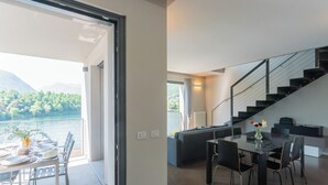 A modern living room with a dining area, a staircase, and a view of a lake. - Mulino Vista Lake by Rent all Como (Tremezzina)