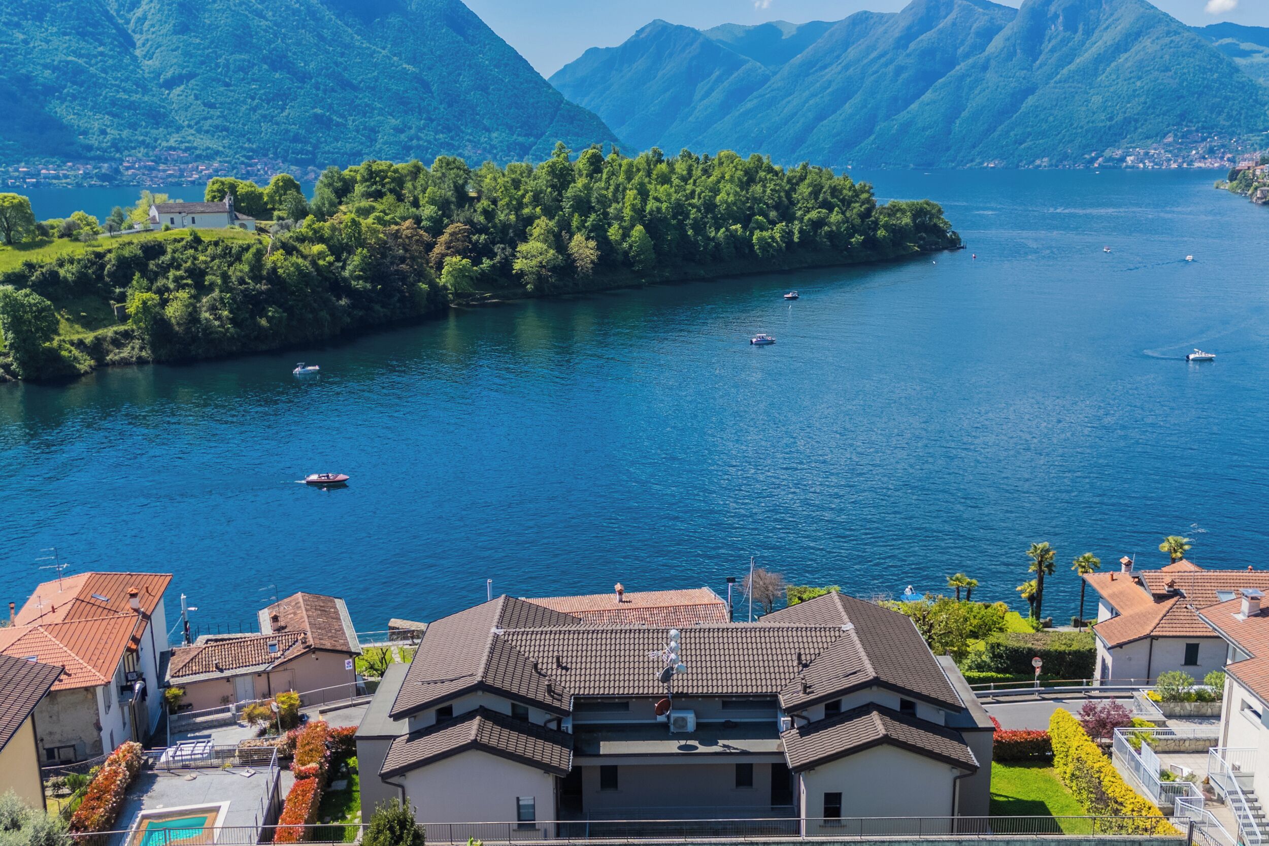 A coastal village with terraced houses, a small island with dense greenery, and boats on the water.