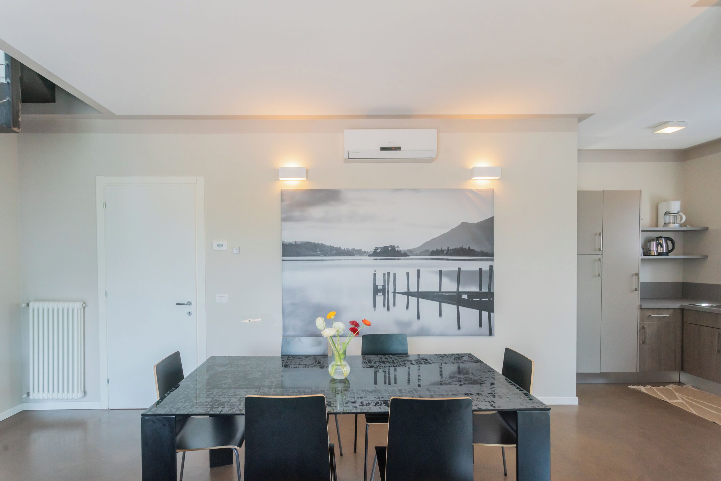 Een moderne eetruimte met een grote tafel, vier stoelen, een vaas met bloemen en een wandairconditioning.