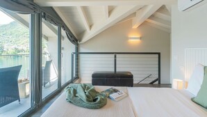 A modern bedroom with a large window, a bed, a reading area, and a balcony with outdoor furniture. - Mulino Vista Lake by Rent all Como (Tremezzina)