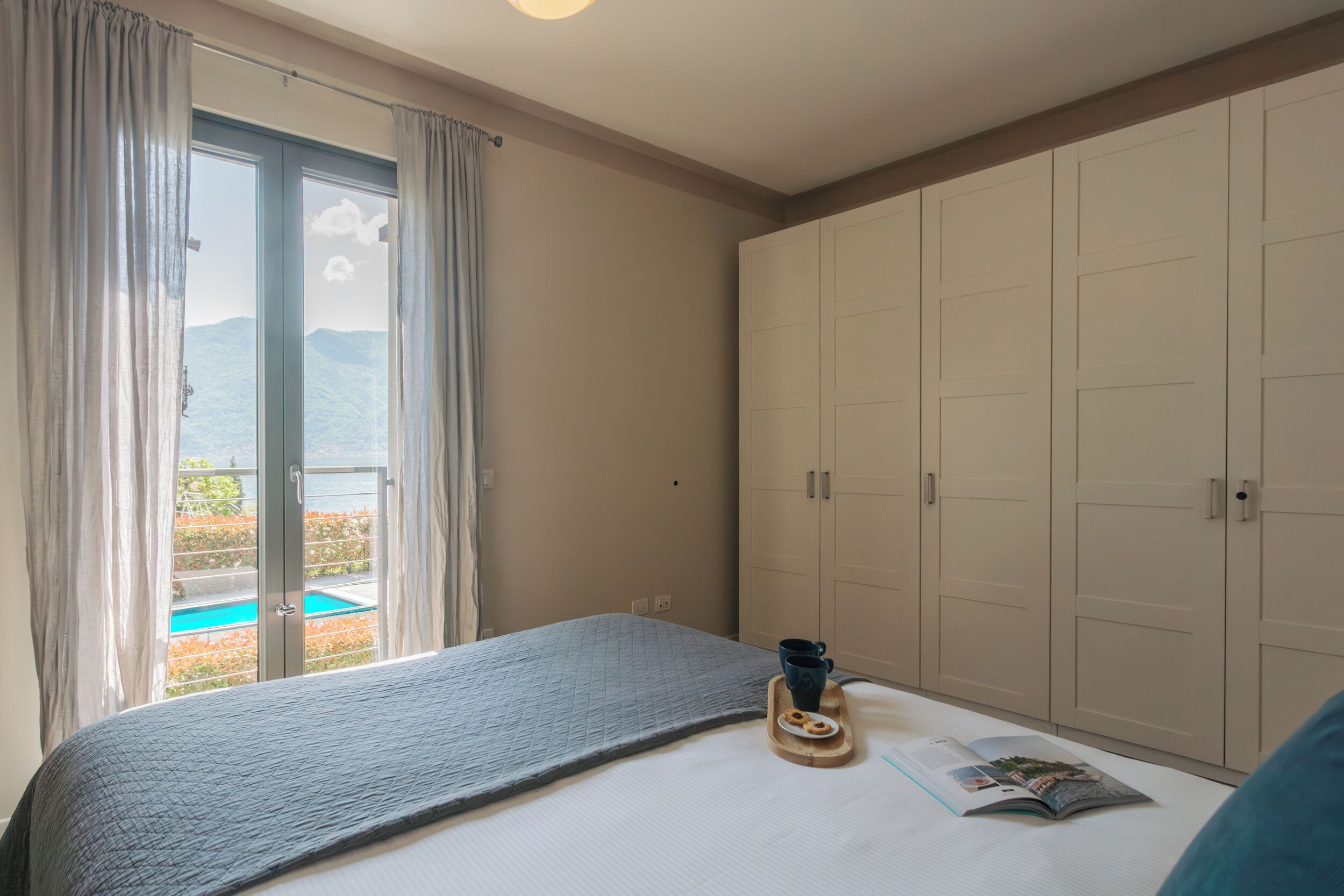 Un dormitorio con cama, ventana con cortinas, vista a una piscina y un armario.