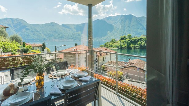 A balcony with a table set for dining, overlooking a lake and mountains. - Mulino Vista Lake by Rent all Como (Tremezzina)
